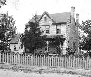 Davie's house. It is two stories, and has a small adjoining build on the left. There are trees in the yard and fence marking the property's bounds.