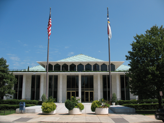 A building with the state and US flag in front. It has several floor to ceiling windows that are blacked out. 